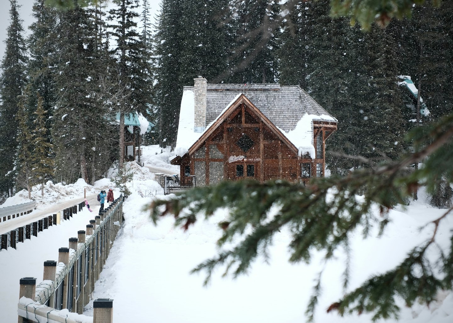 Wooden lodge in snowy evergreen forest with people on boardwalk.