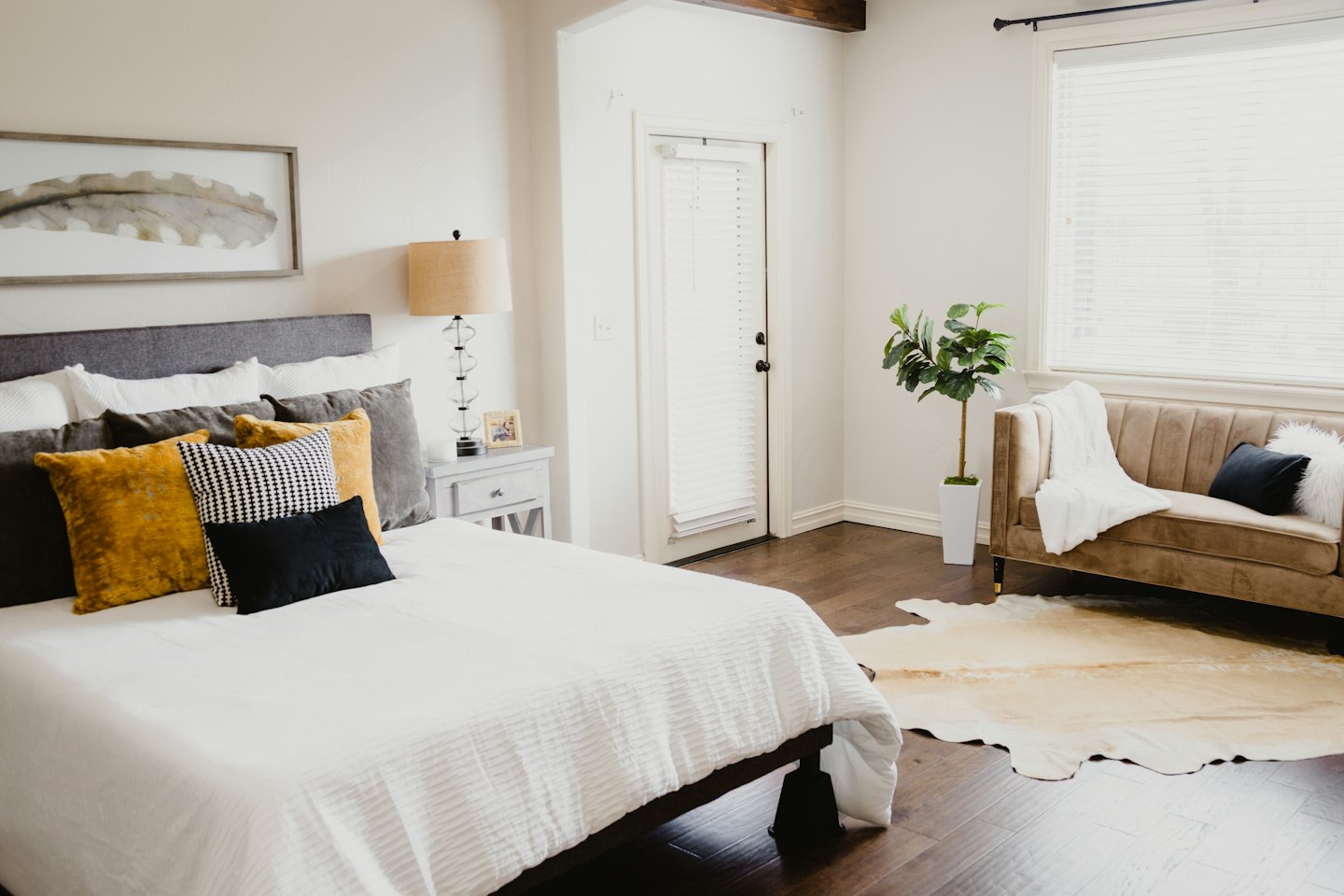 Cozy bedroom with a made bed, dark wood floors, and natural light.