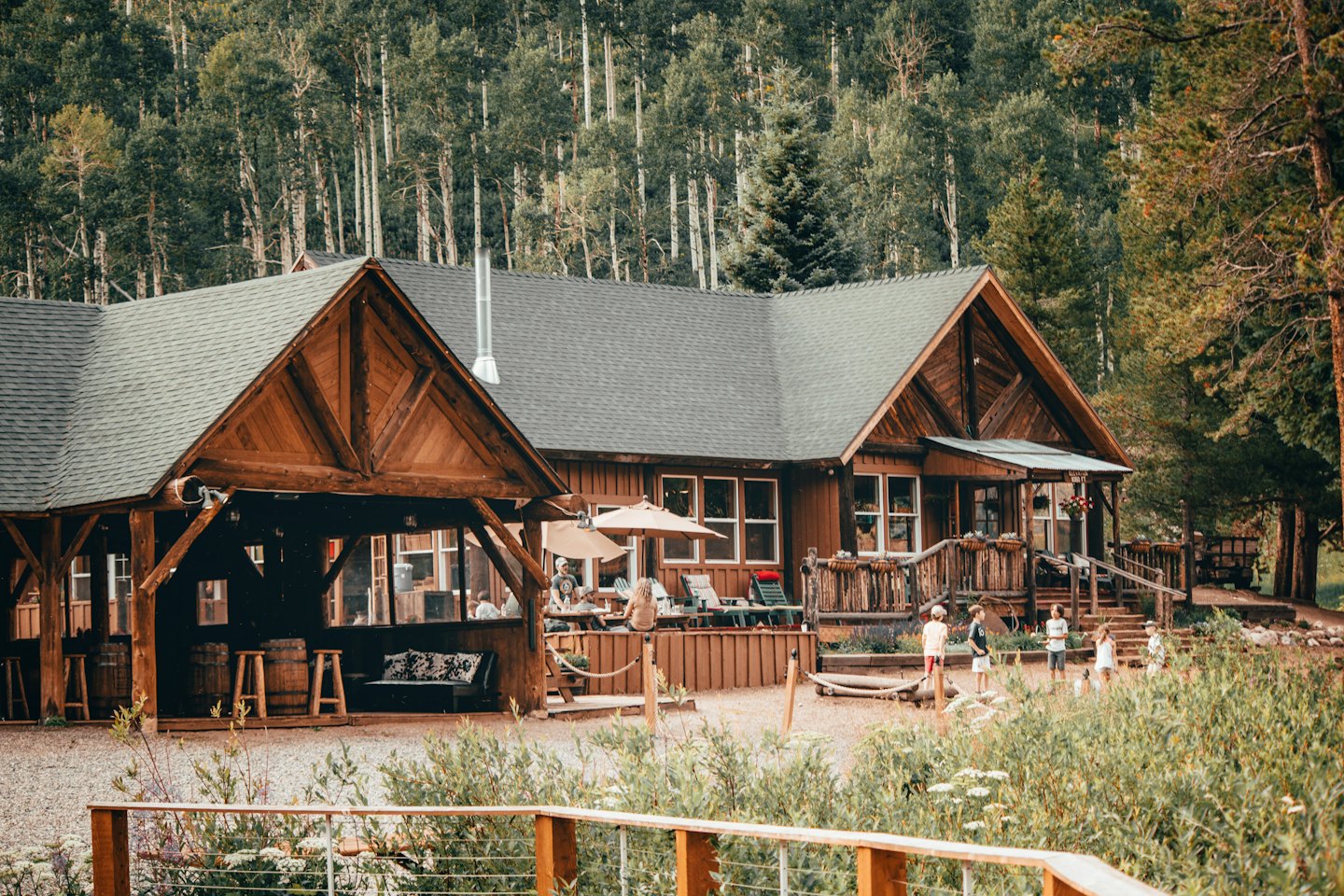 Wooden lodge at base of forest with people on deck.